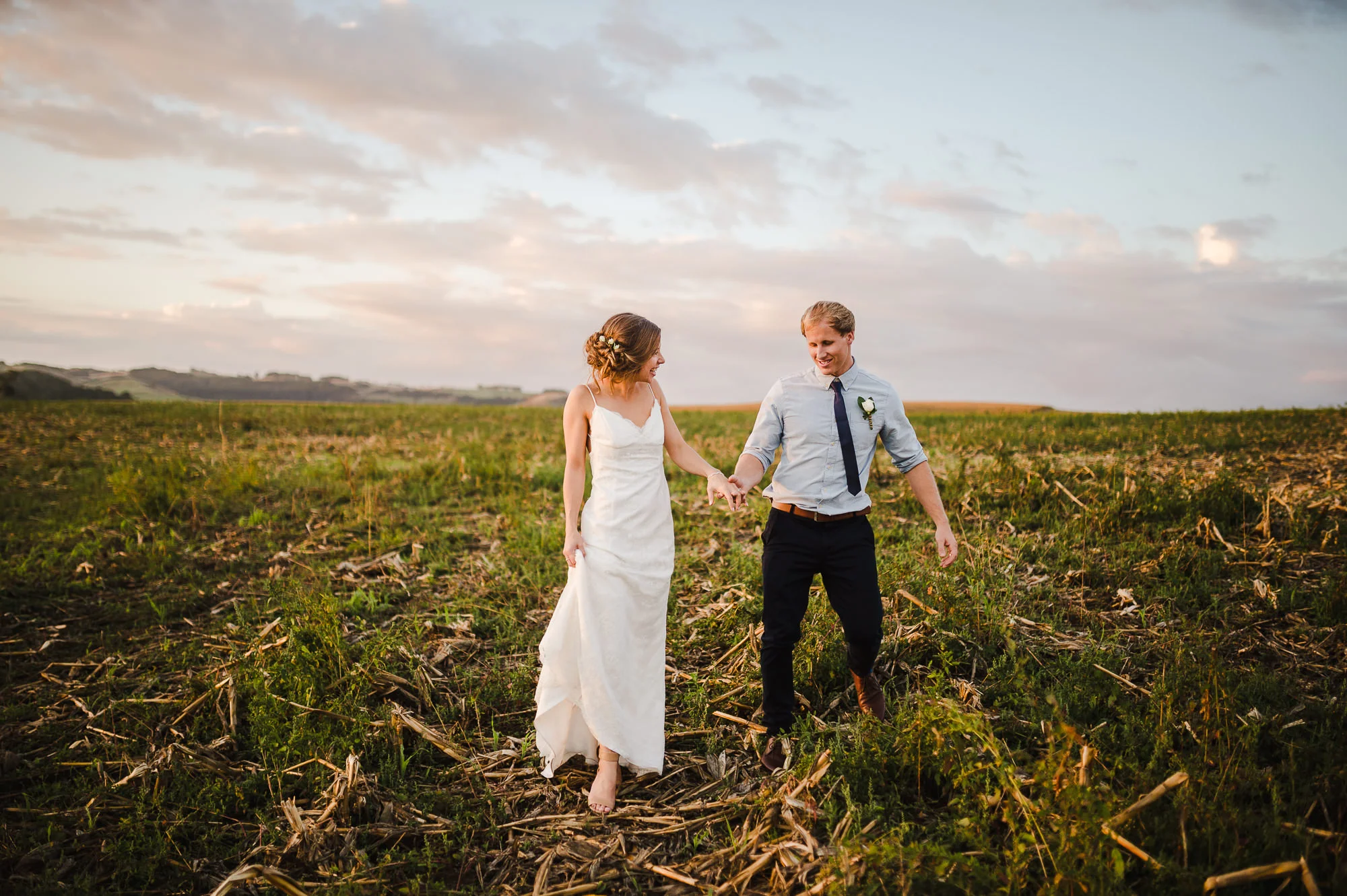 wedding couple walking through corn field at sunset.jpg