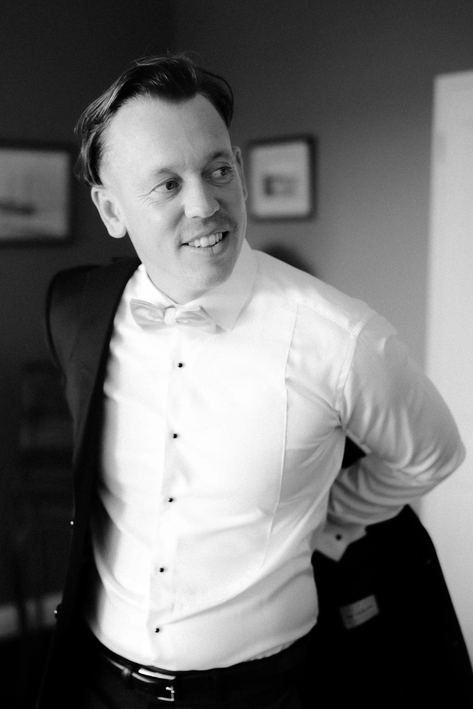 Black and white image of groom putting jacket on
