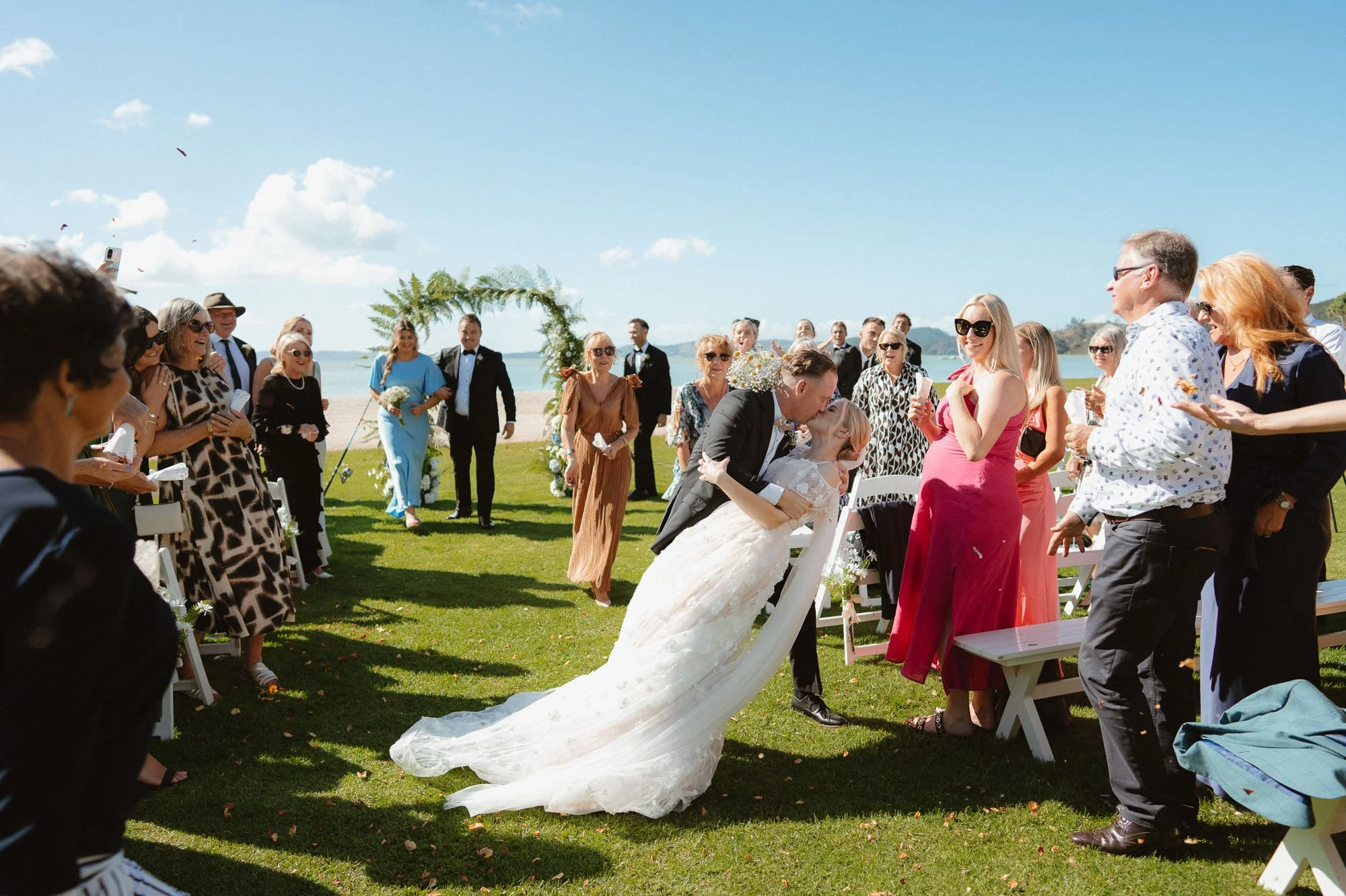 Aisle dip kiss, The McCallum Residence beach in background, sunny ceremony