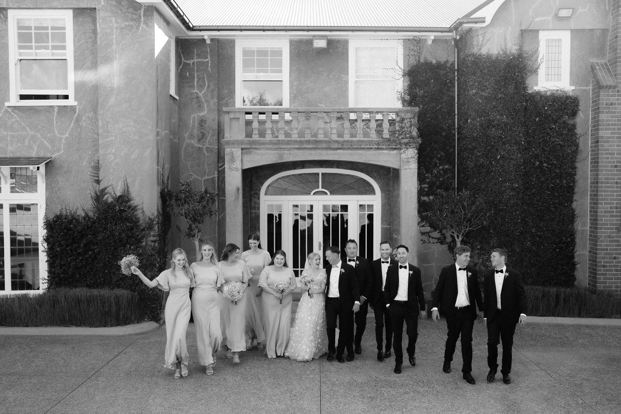 Black and white image of bridal party walking towards camera in front of The McCallum Residence