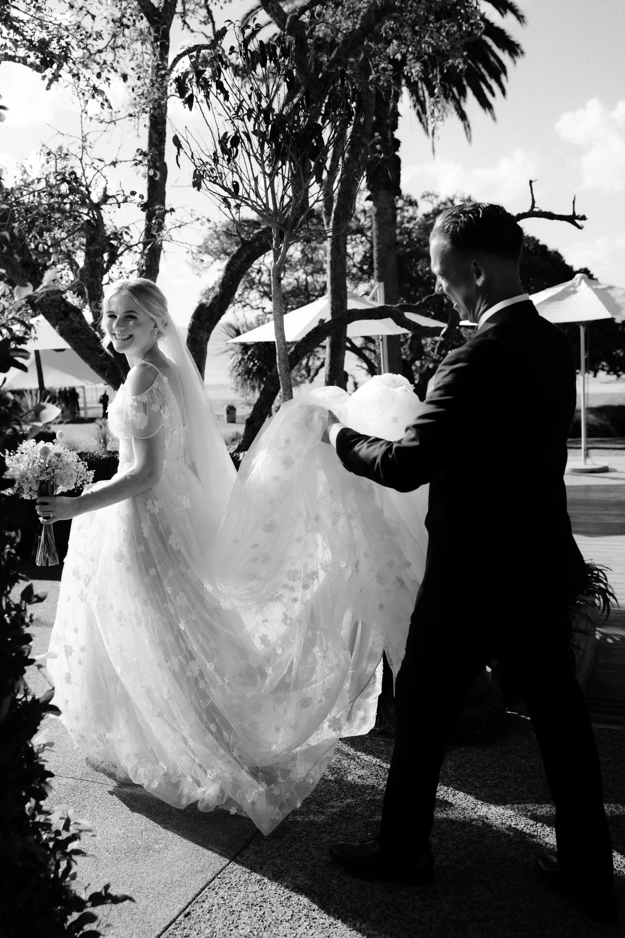 Black and white moment of bride with groom carrying dress while walking