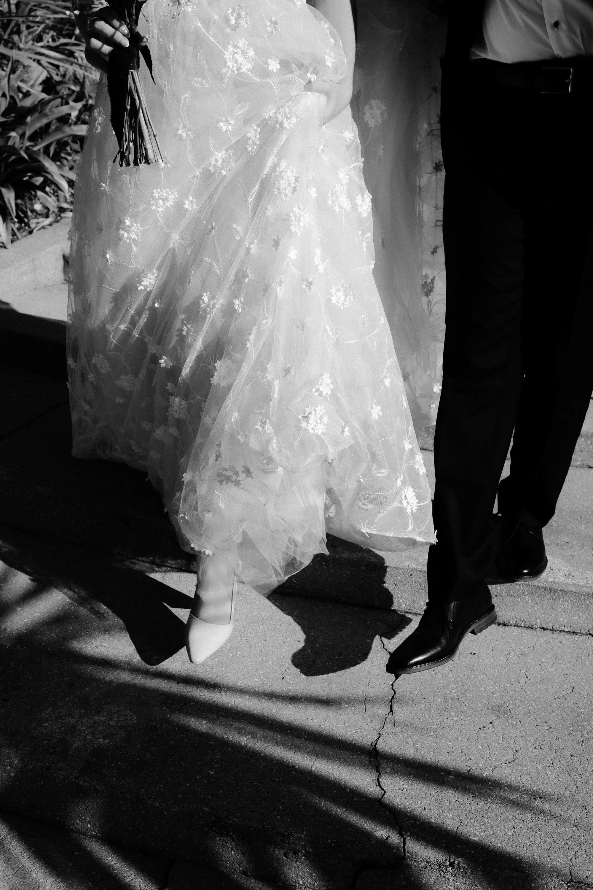 Detail shot of bride and groom's shoes walking in contrasty light