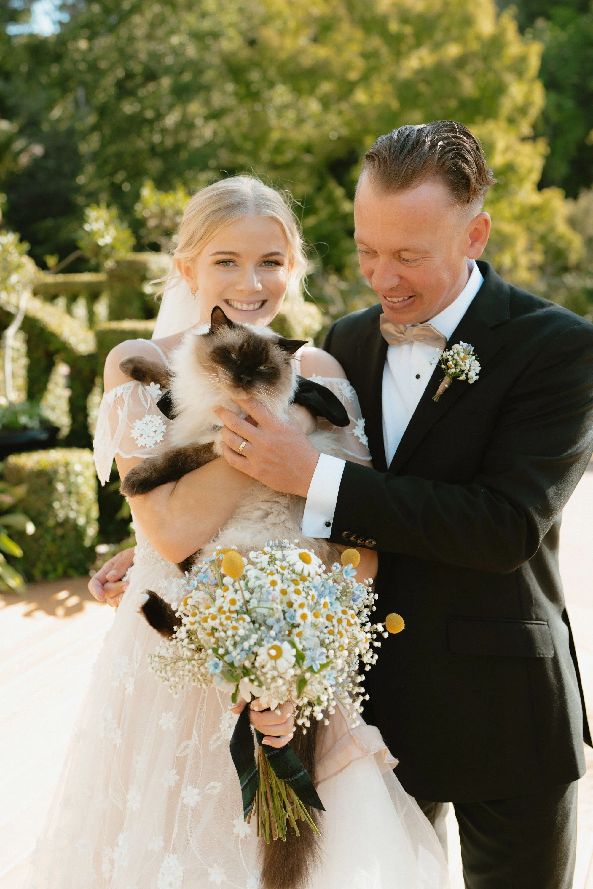 Bride and groom cuddling cat in tuxedo