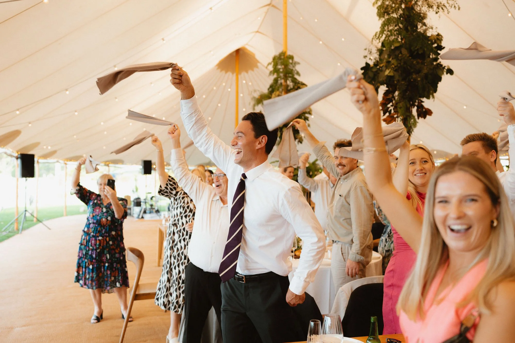 Guests excitedly waving their napkins to welcome bride and groom in marquee