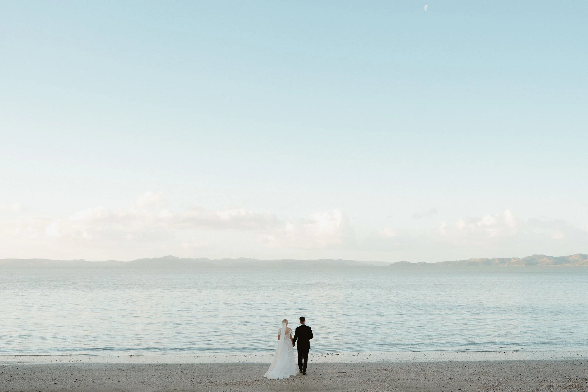 Sunset portrait, wide shot of beach and bride and groom having a moment together at The McCallum Residence