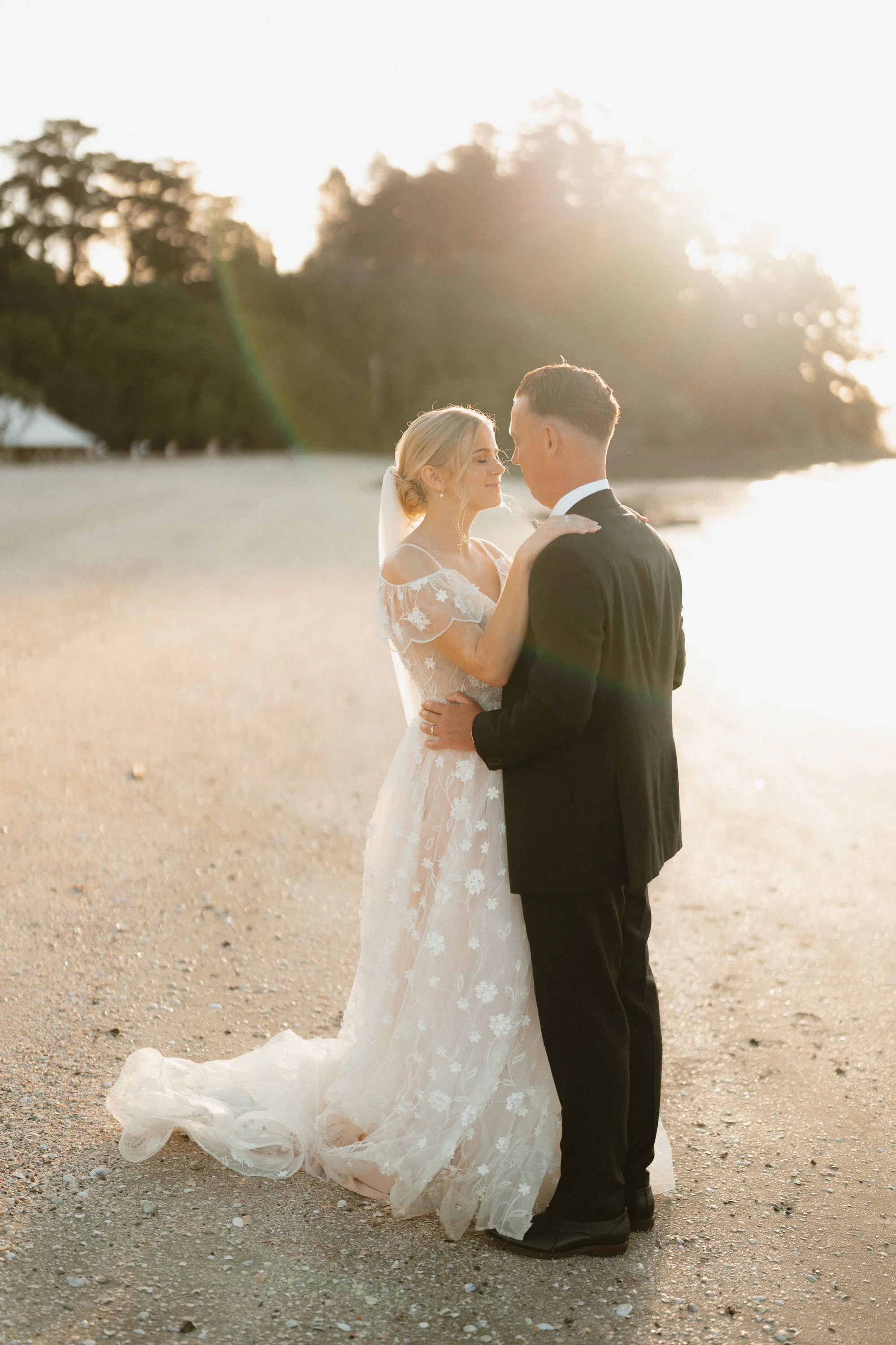 Sunset backlit photo of bride and groom cuddled together on beach at The McCallum Residence