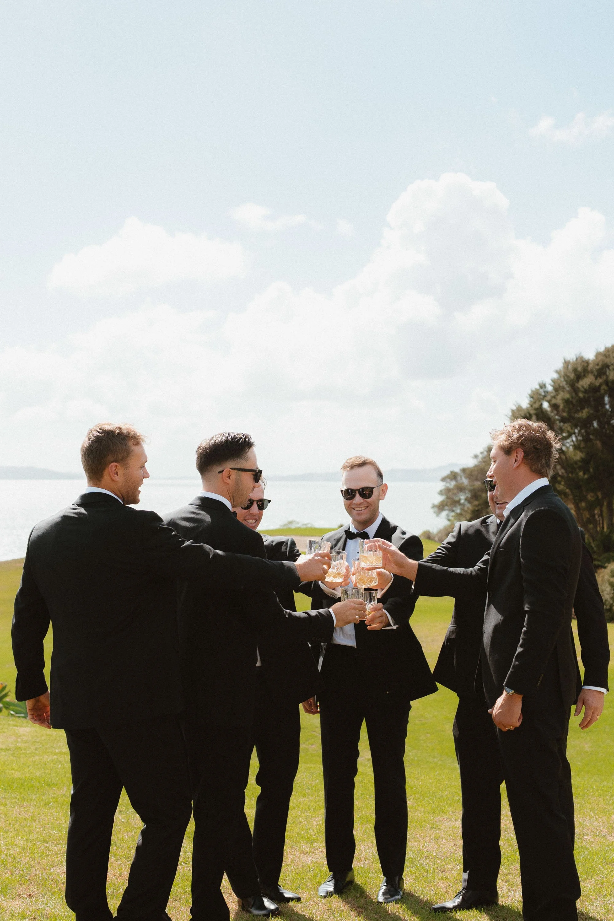 Groomsmen cheersing their drinks in suits at Tio Point Accomodation