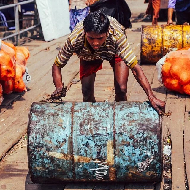 Archive: From my first trip to Yangon, Myanmar. A young man rolls a barrel from the hold of a recent arrival to port. Notice he uses a handful of grass in the place of gloves to protect his hands. The world has changed so much since this photo, but I