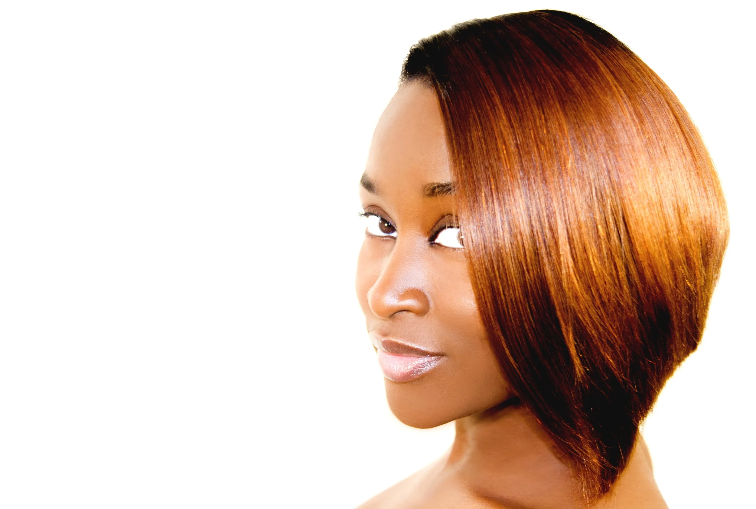 A woman with sleek, straight, reddish-brown hair in a layered bob style, looking over her shoulder with a slight smile against a white background.