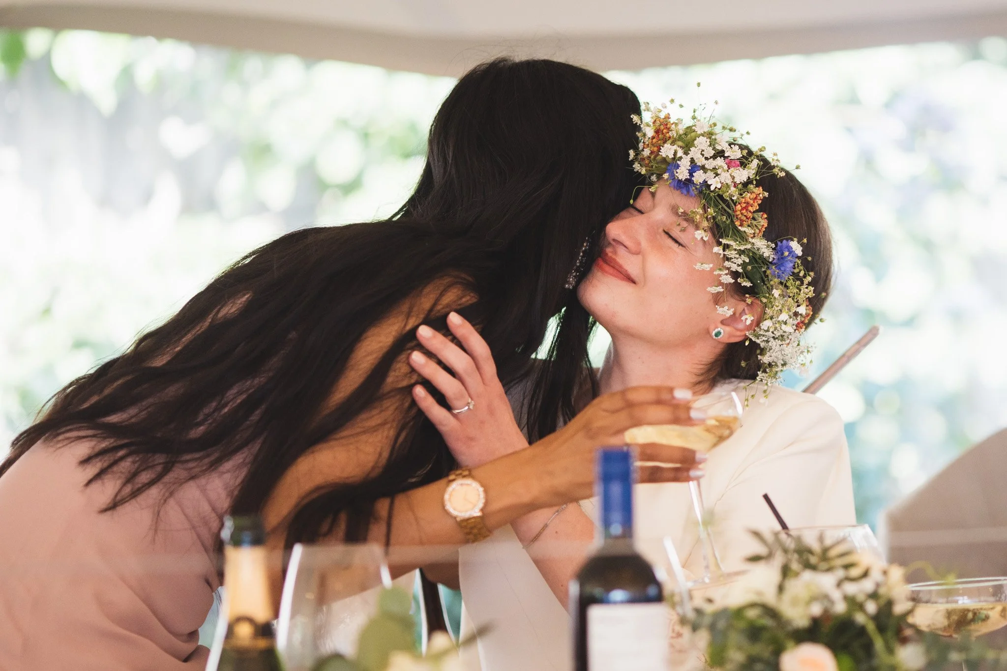 The bride and maid of honour share an emotional hug after her speech. The bride wears a flower crown.