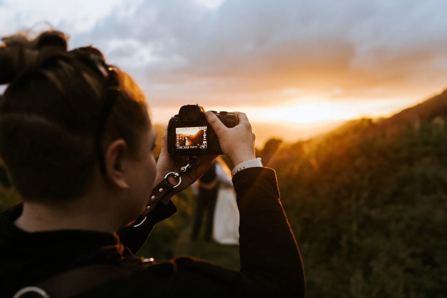 Cat Lane taking a photo of a bride and groom in a brilliant seaside golden hour with hills and cloudy sky.