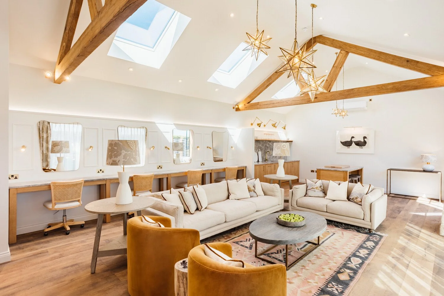 The inside of the Apple Shed at South Farm. The room features a makeup station, sofas and coffee table and kitchenette. Star shaped lamps hang from the ceiling and blue skies can be seen through the skylights.