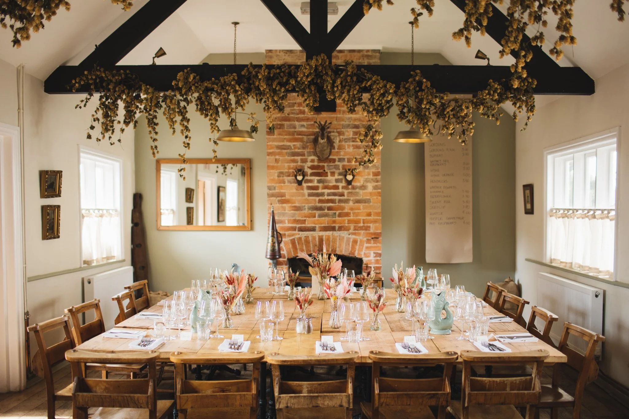 A function room dressed up for a wedding at The Sun in Felmersham in Bedfordshire. Dried hops hang from a ceiling above a wooden table set up for a wedding.