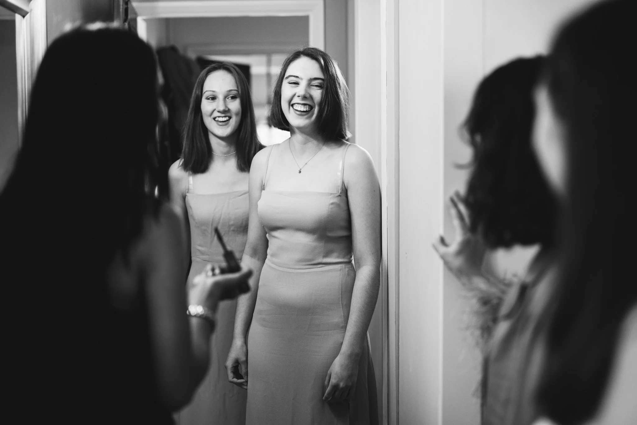 Two bridesmaids smile widely as the bride sees them in their dresses for the first time.