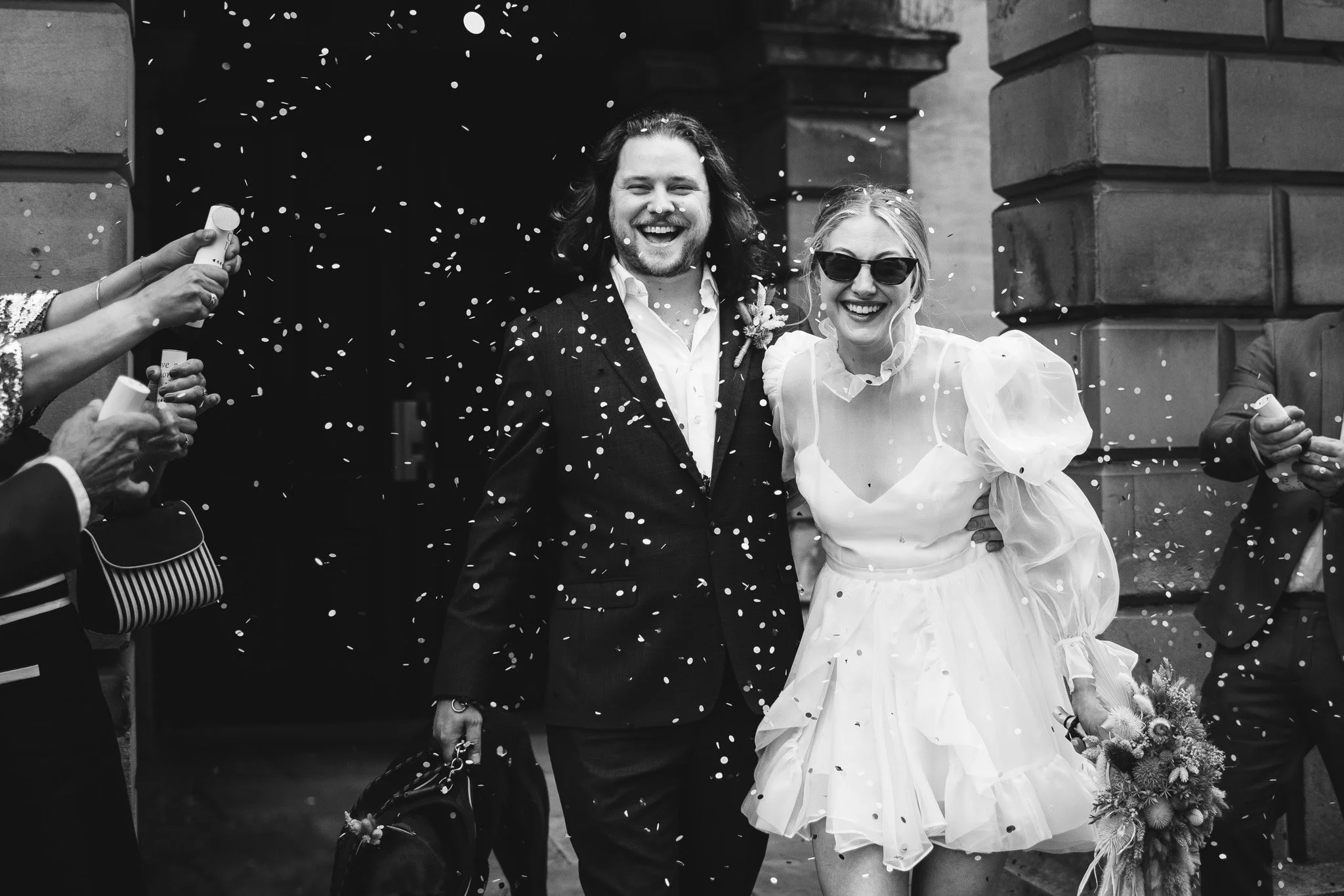 A black and white confetti moment after a micro wedding at Bedford Town Hall. The bride wears a ruffled dress and sunglasses.