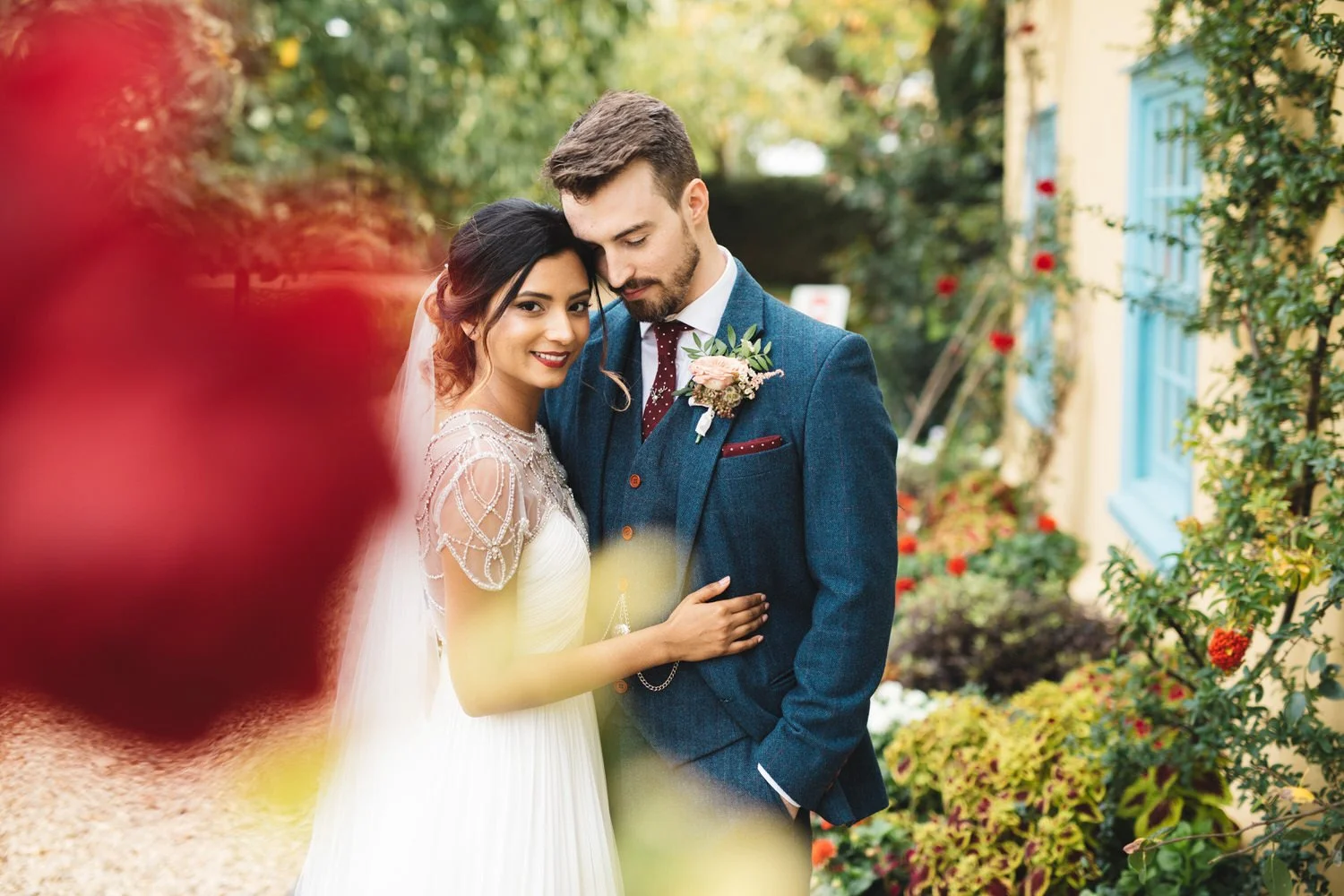 A bride and groom embrace outdoors on their wedding day at South Farm in front of the red roses on the farmhouse.