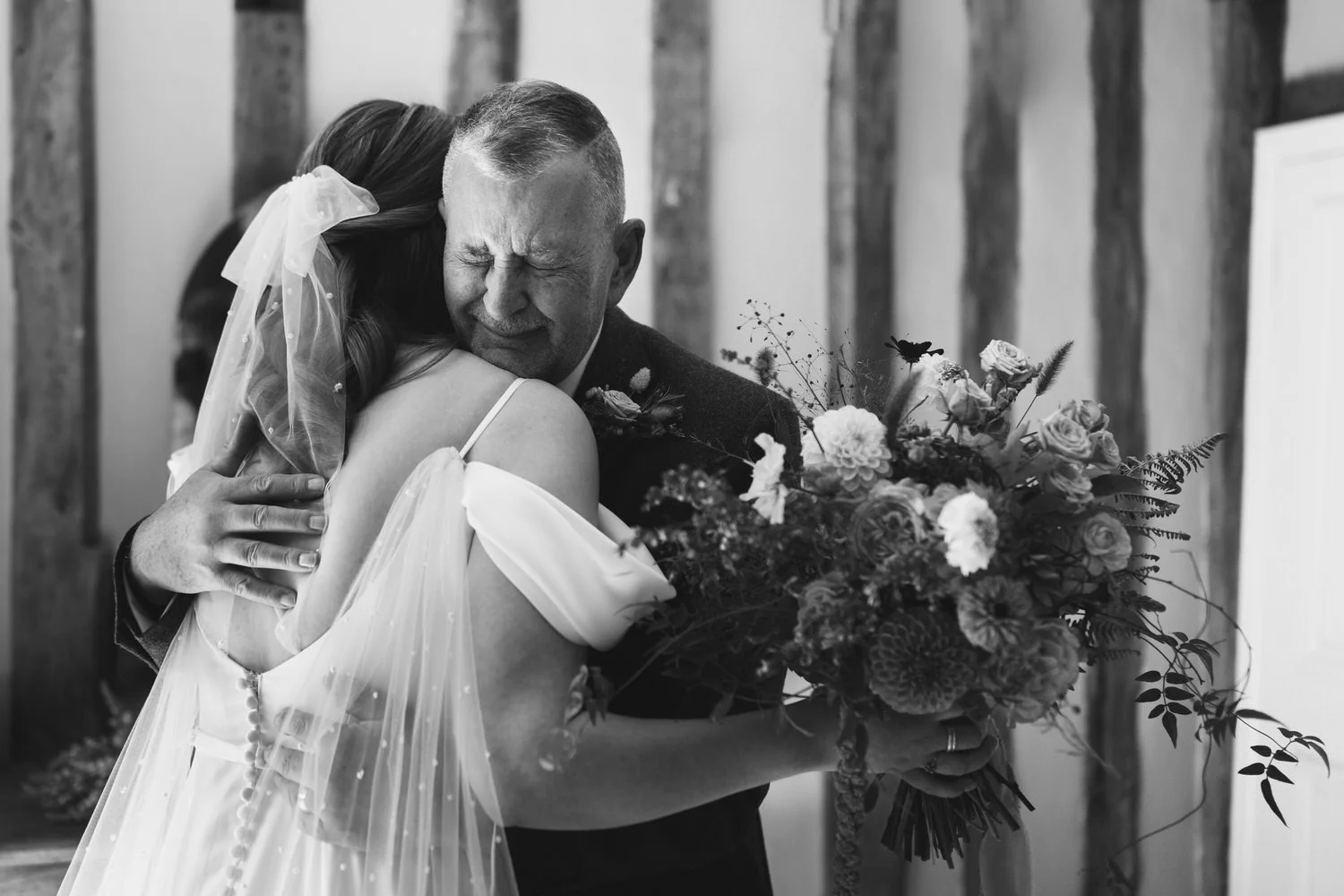 A black and white moment, the father tightly hugs his daughter on her wedding morning after seeing her in her outfit for the first time. He is holding back tears and she has a tulle bow in her hair.