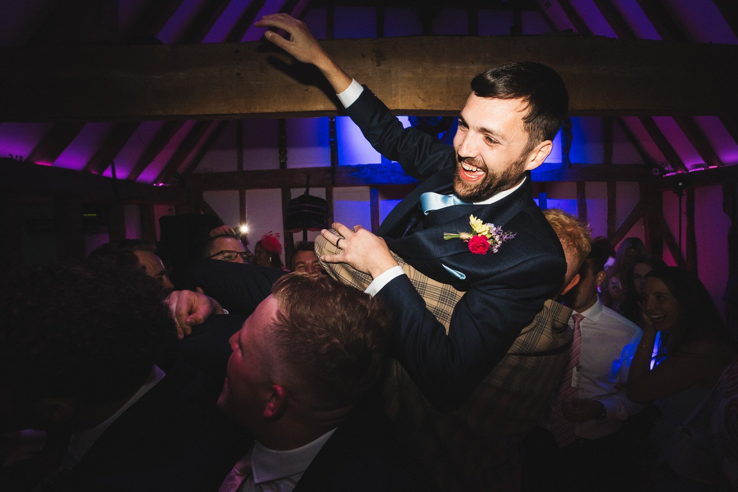 The groom laughs as his friends lift him in the air on the dancefloor.