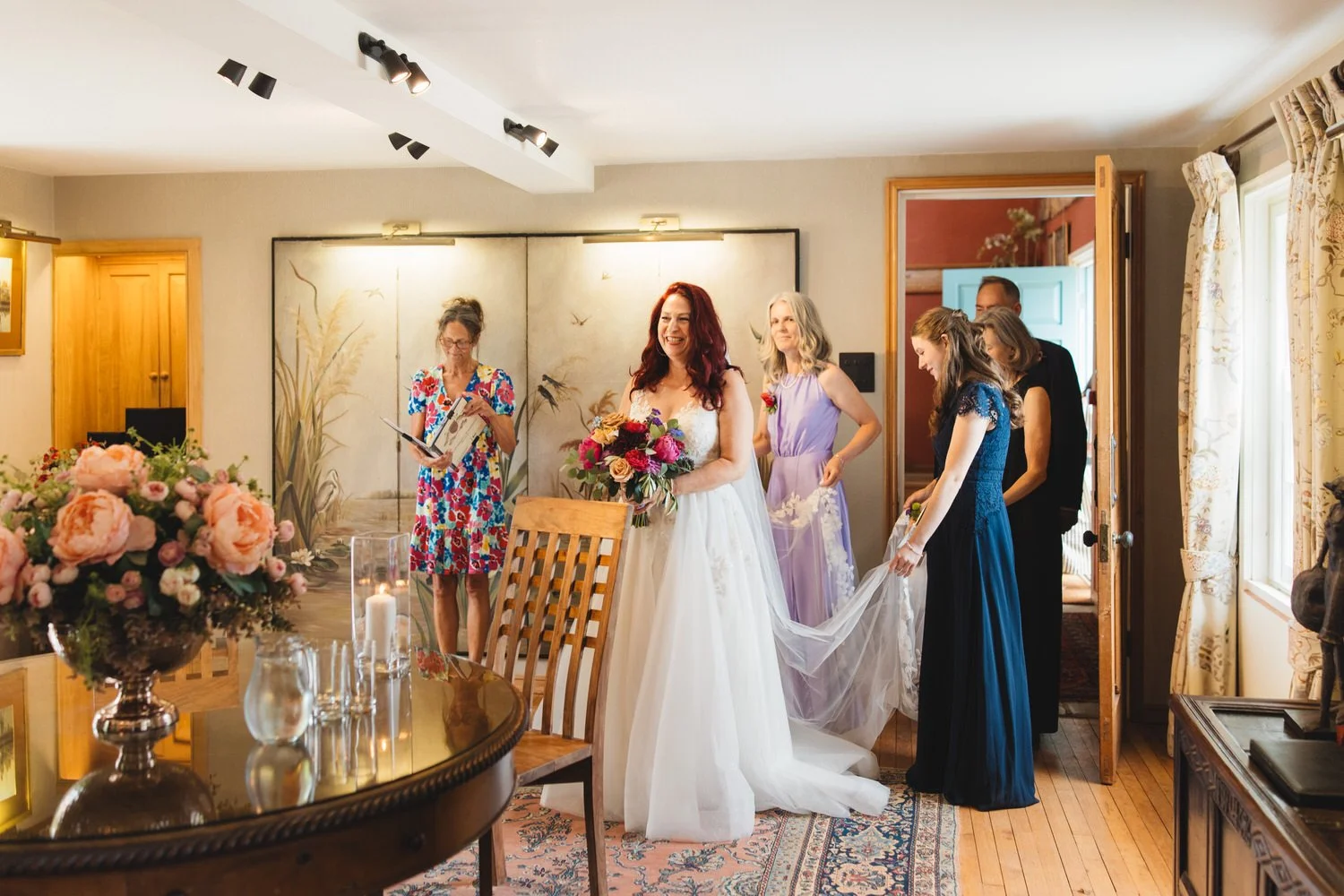 A red-headed bride smiles as her bridesmaids follow her into the Drawing Room at South Farm for the wedding ceremony.