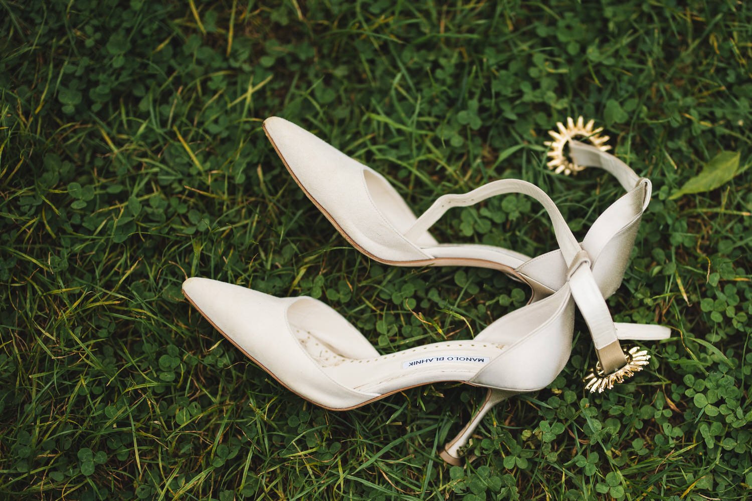 A pair of Manolo Blahnik wedding shoes, tossed aside on the grass on a wedding day.