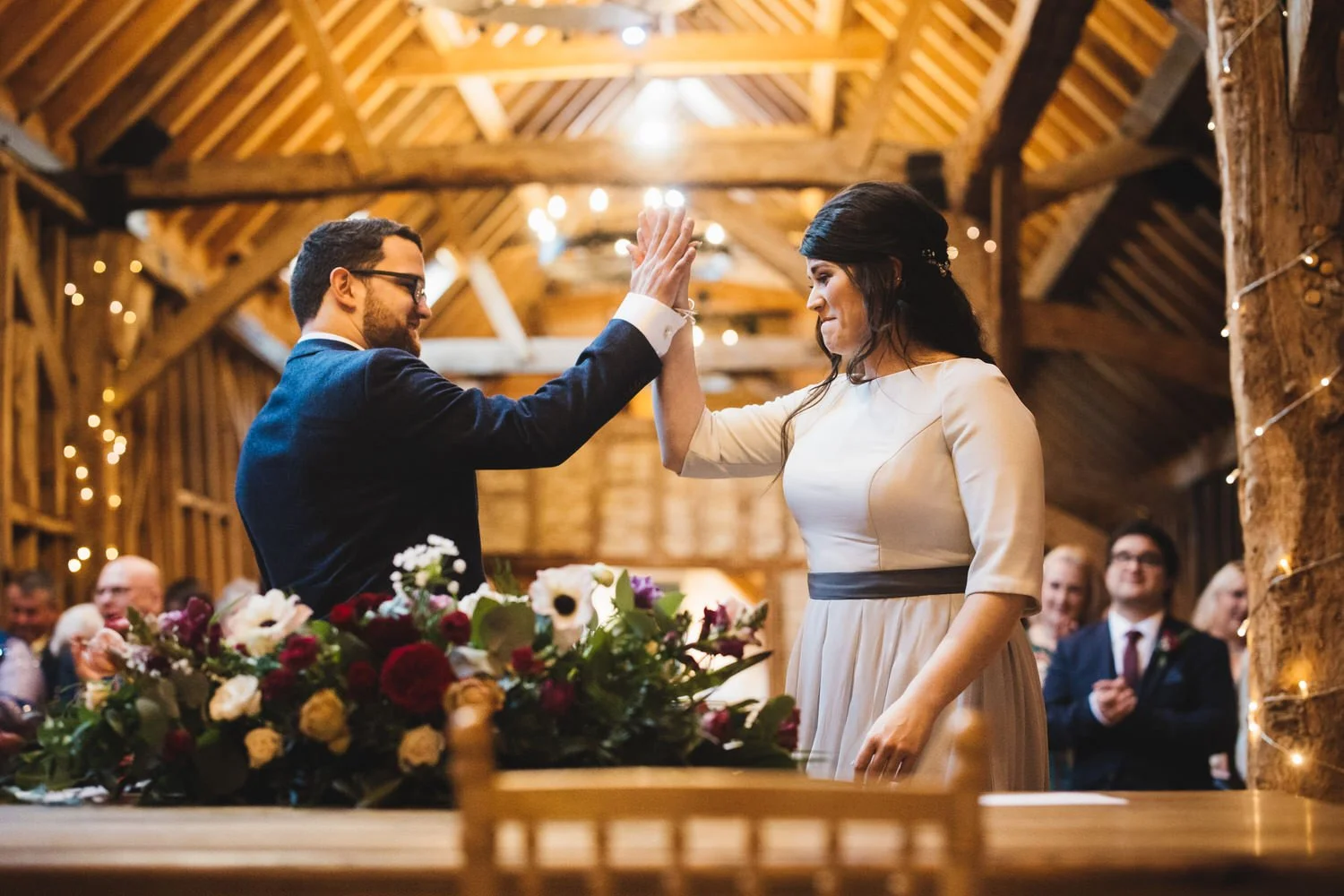 A couple high five at the end of their wedding ceremony at Bassmead Manor Barns as their guests look on.