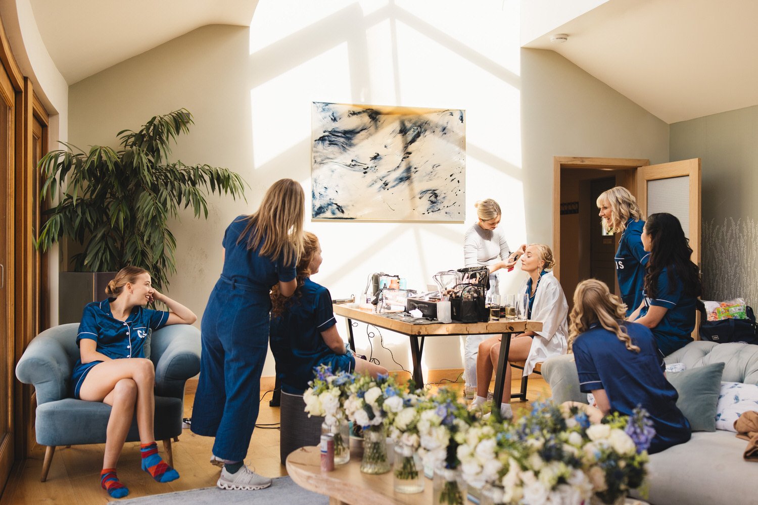 A wide angle view of the Fen Bridge Farm B&B living room.  Sun pours in through the sunlight as the bride has her makeup done and her bridesmaids and mother look on, smiling.