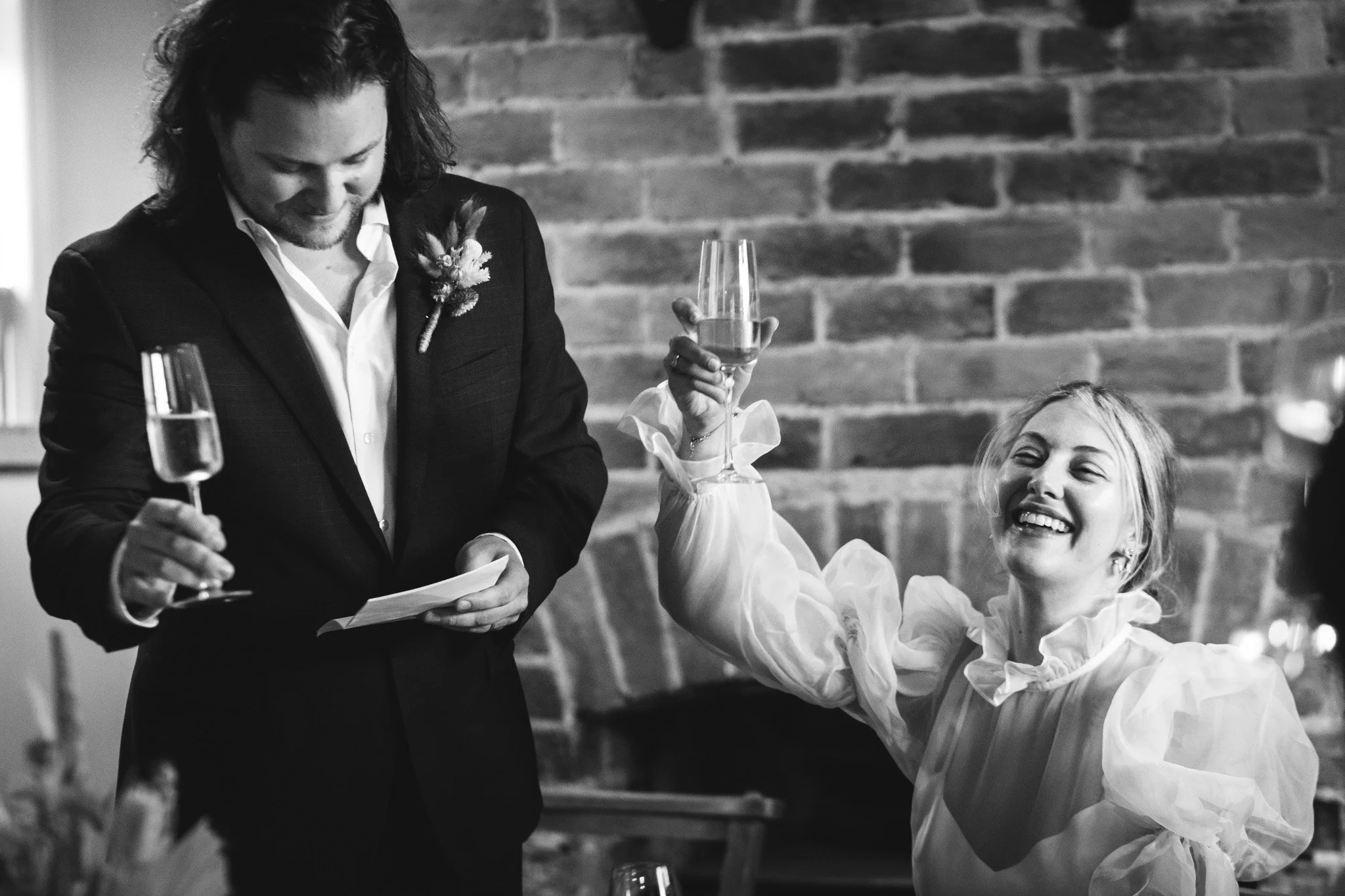 A black and white shot of a bride and groom joyfully toasting at the end of the groom's speech during their micro wedding in Bedfordshire.