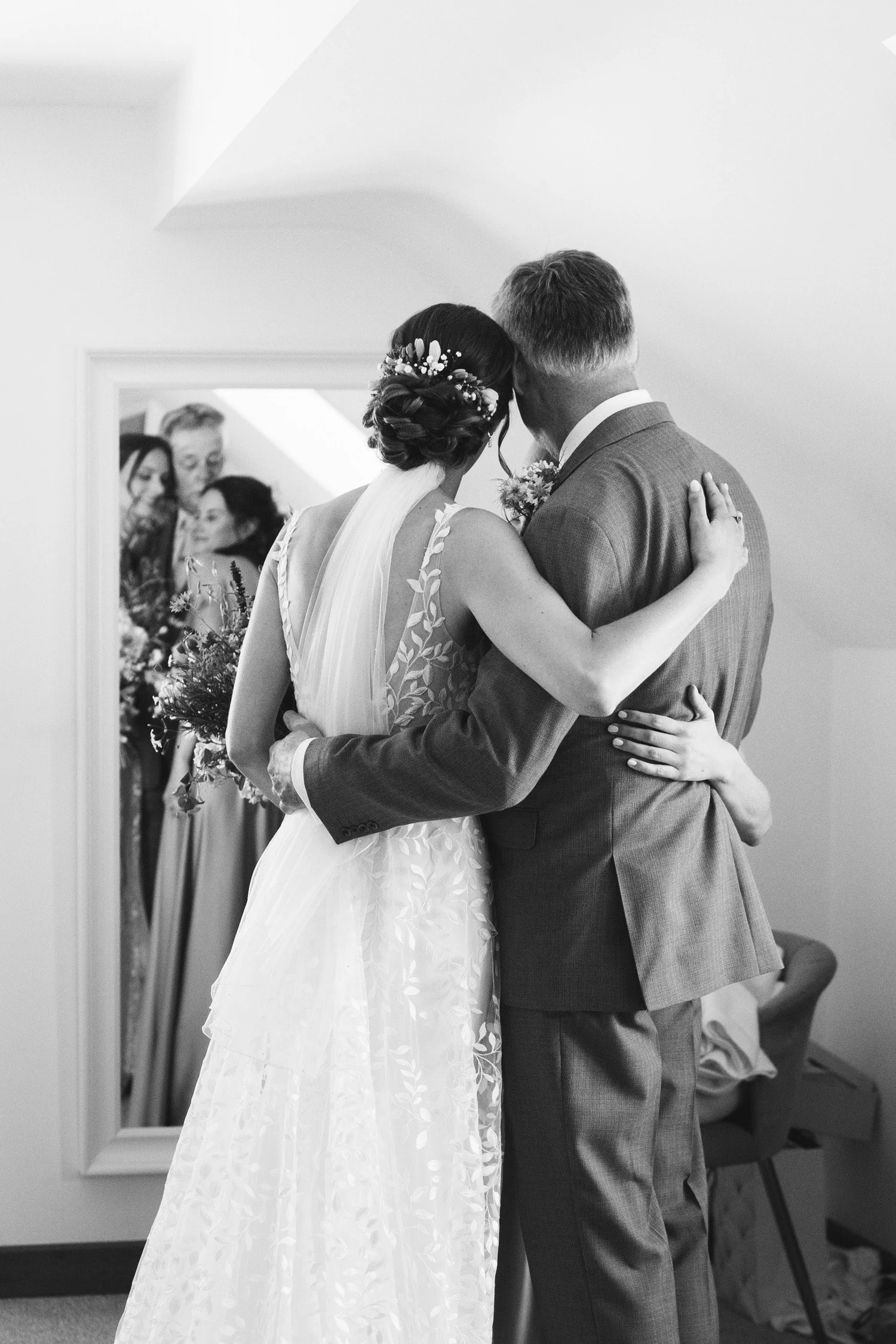 The bride, her father and sister share a hug before the ceremony in black and white.