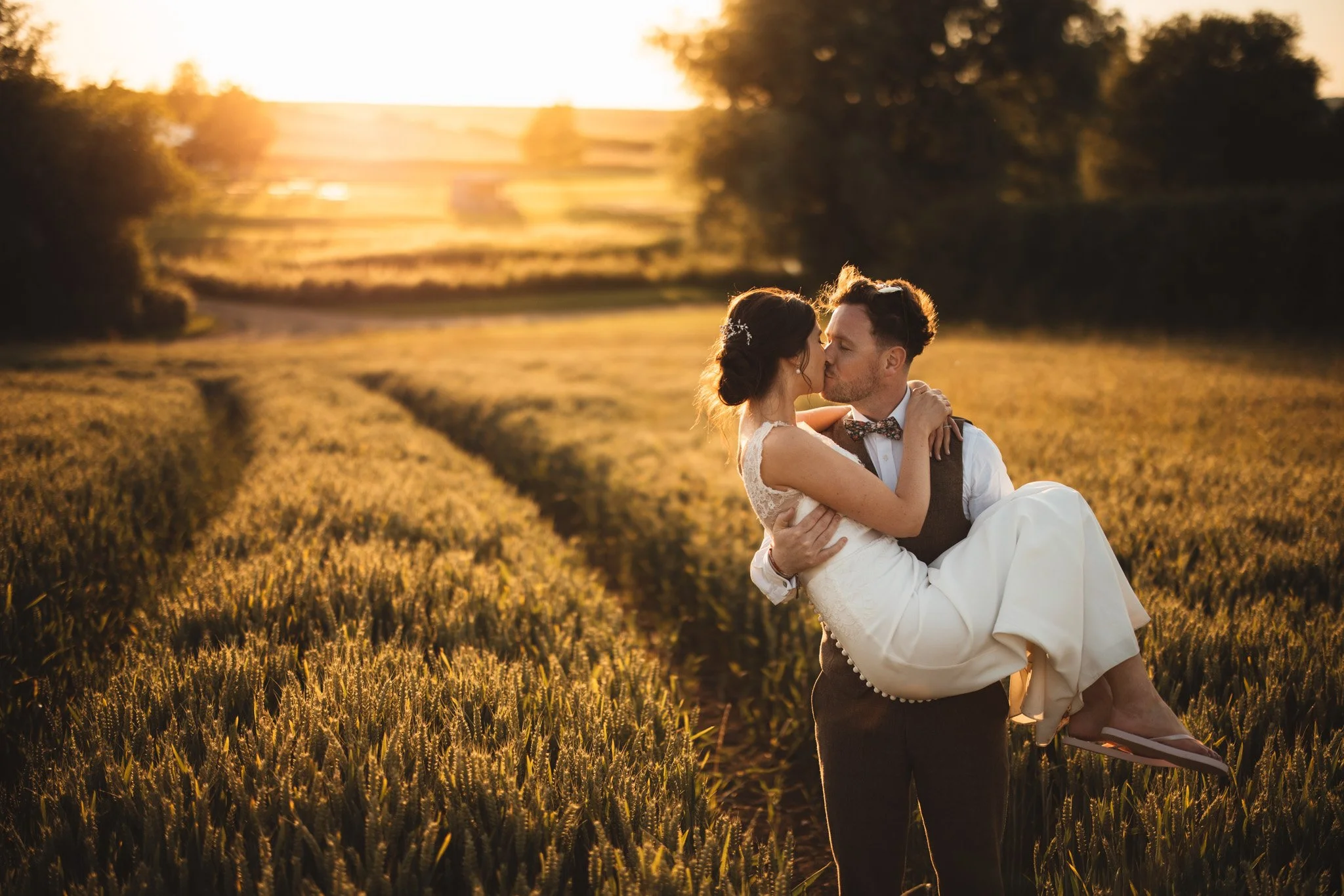 In the golden hour sun, Alex and Matt share a kiss as he lifts her up in a wheat field in Bedfordshire.