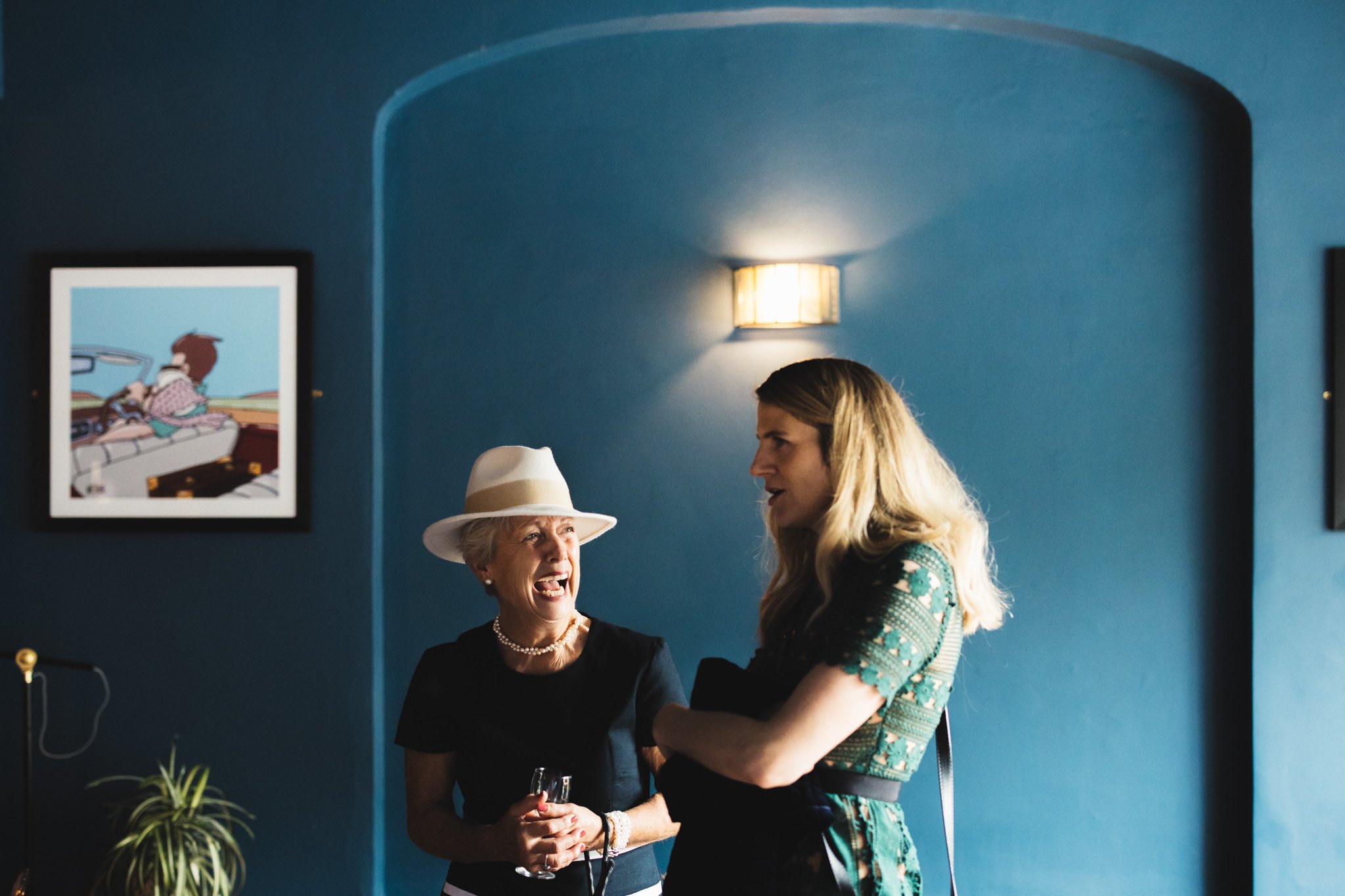 In a cocktail bar, a wedding guest laughs as she talks to another guest.