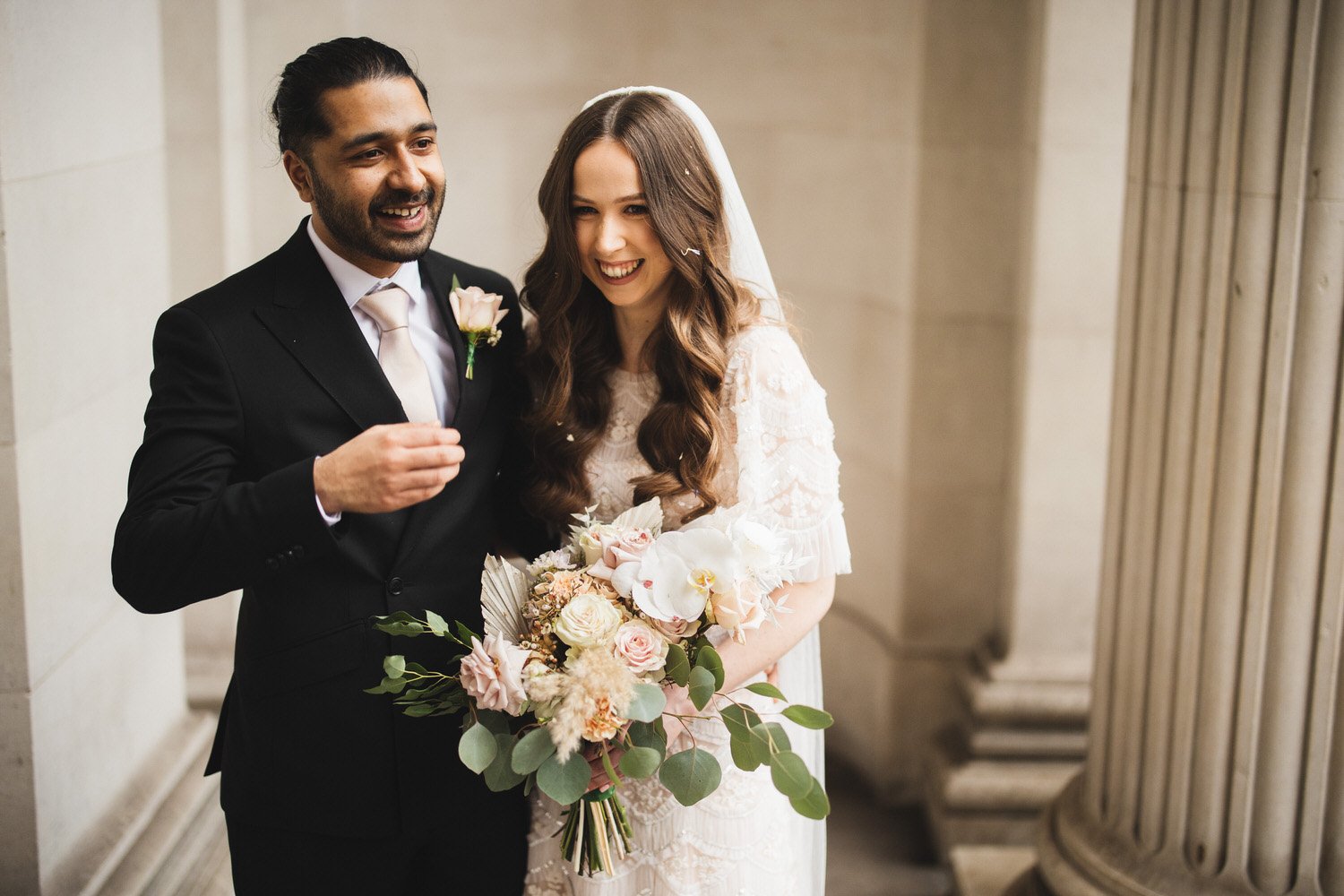 After their ceremony, a couple laugh in front of the pillars at Old Marylebone Town Hall.
