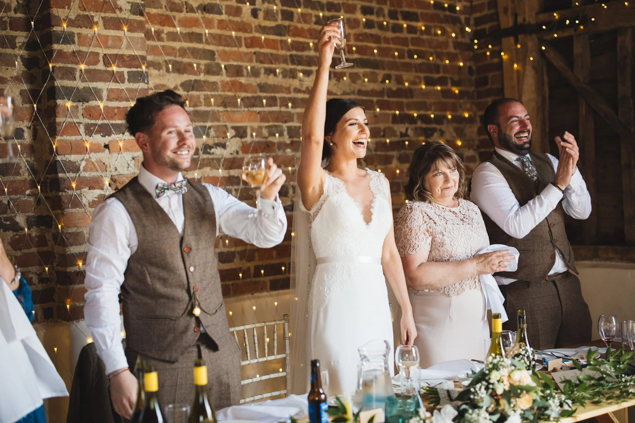 The bride, groom and the people on the top table lift their glasses up to toast at the end of a speech.