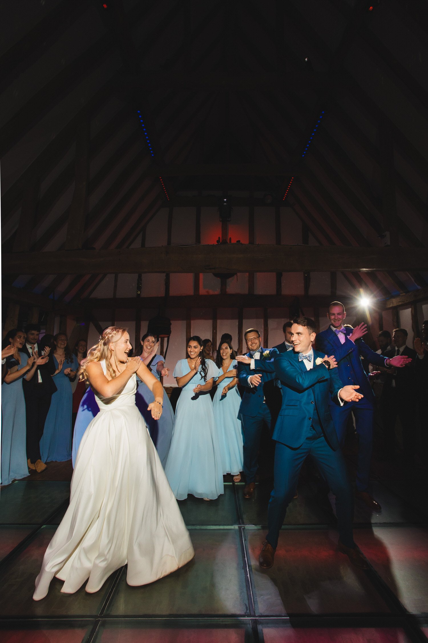 The bride and groom look at each other smiling as they dance the macarena on their wedding dancefloor.