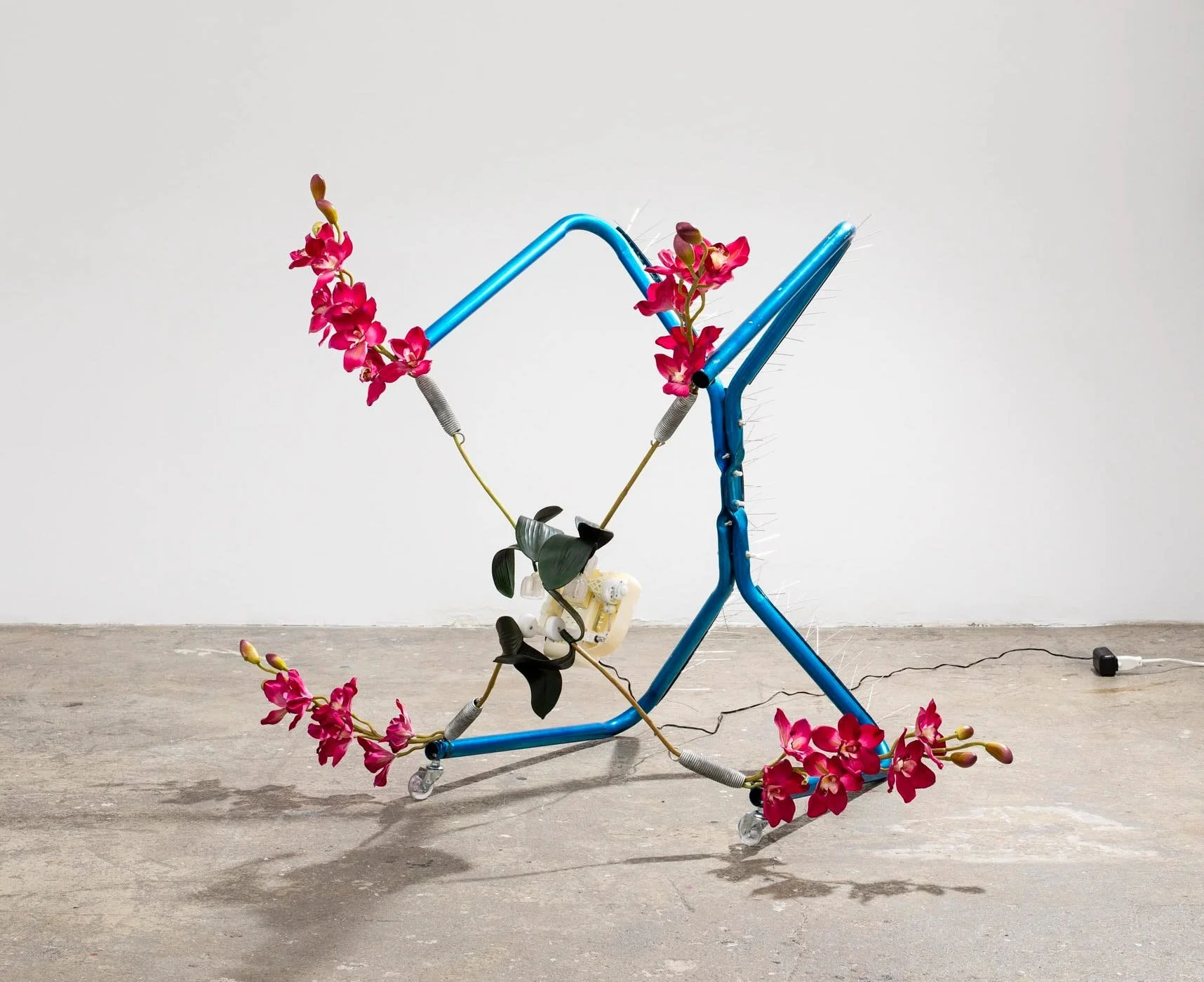 Rachel Youn, Endure, 2023. Spring horse frame, shiatsu neck massager, artificial orchids, polyurethane swivel casters, stainless steel bird spikes. 35 × 25 × 40 in.