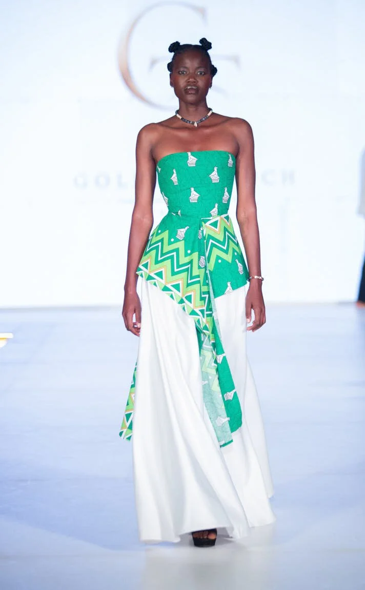 Model walking the runway in a strapless green patterned dress with a long white skirt.