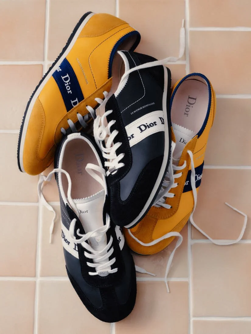 Yellow and black pairs of Dior Ribbon sneakers on peach-coloured tiles.