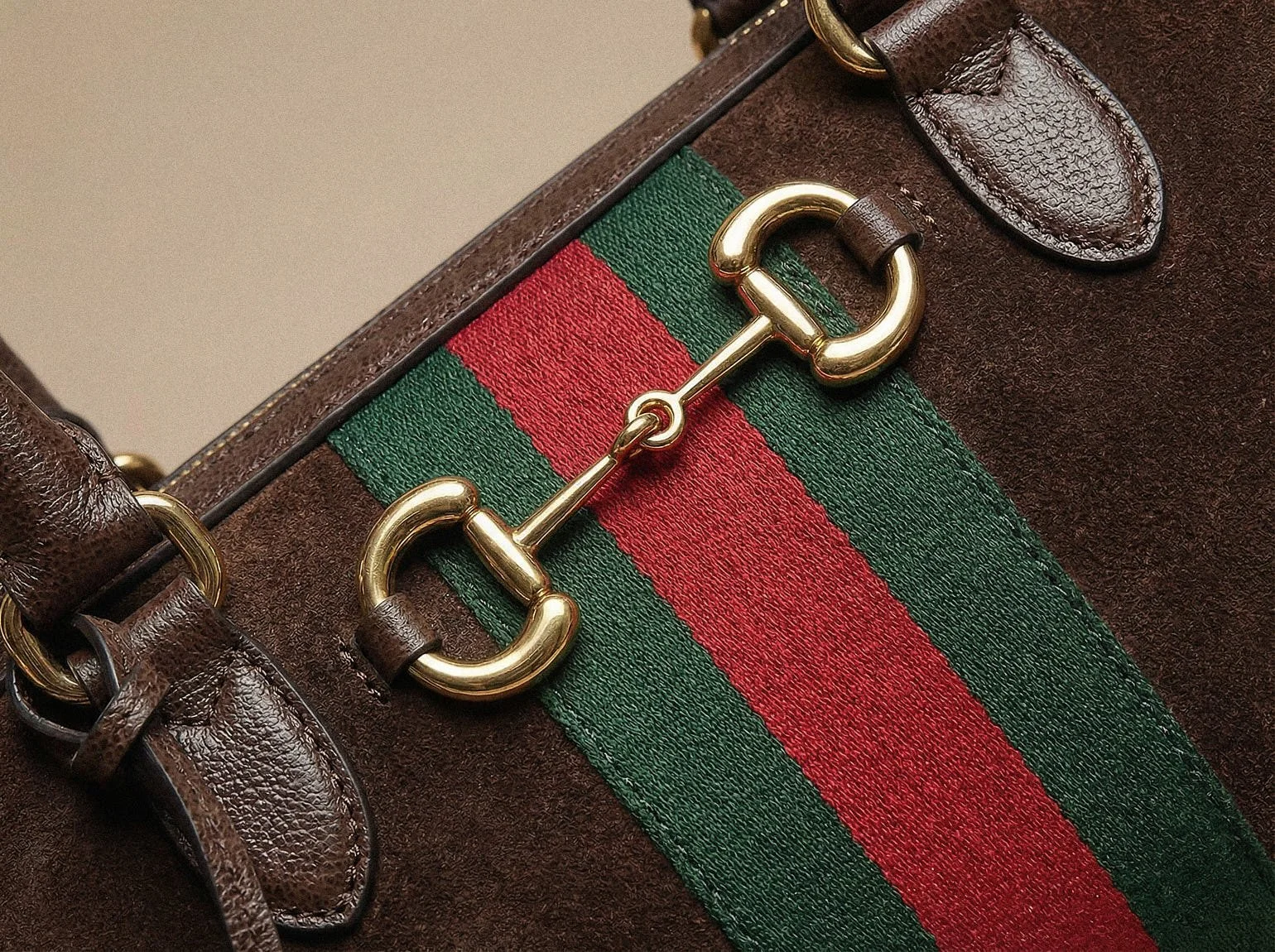 Close-up of a brown suede Gucci Borsetto bag with gold Horsebit hardware, green-red Gucci Web stripe and dark brown leather handle details