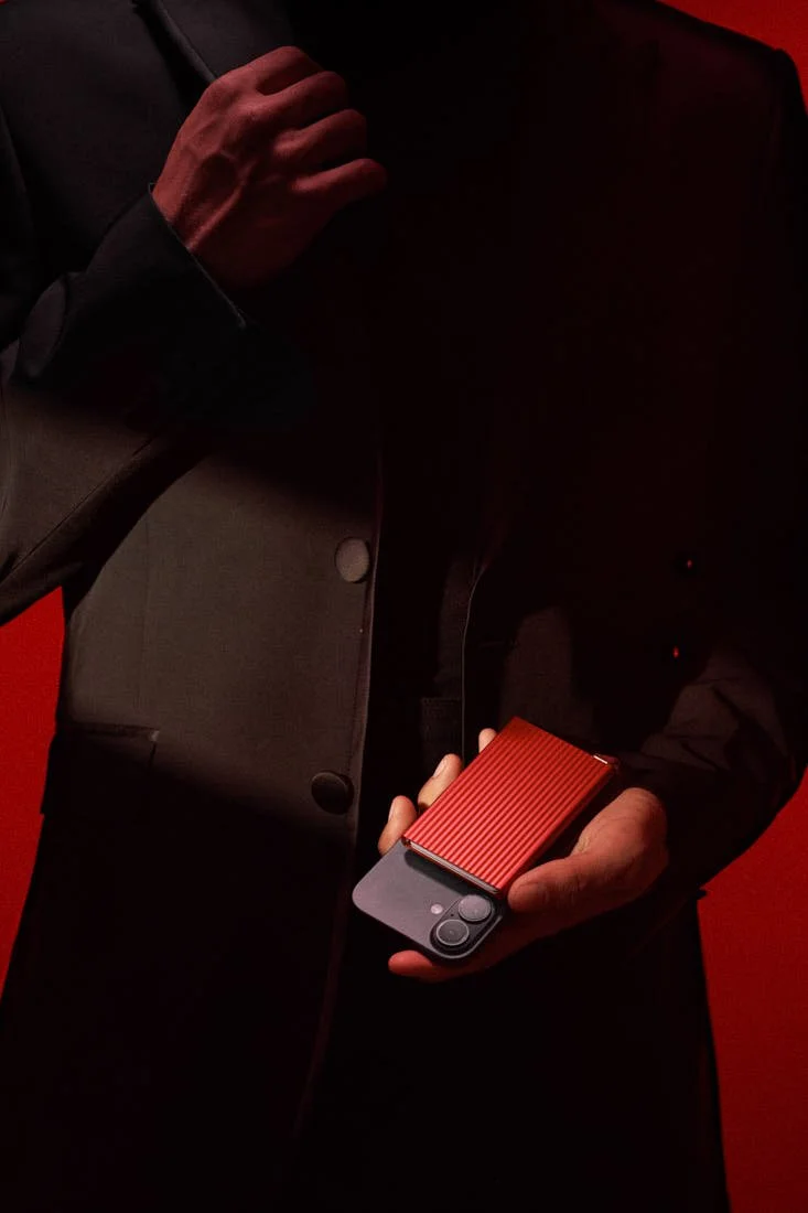 SECRID Premium Cardprotector+ Fluted for MagSafe in red attached to a black smartphone and held in hand, showing its ridged aluminium surface and compact profile, LE MILE Magazine.