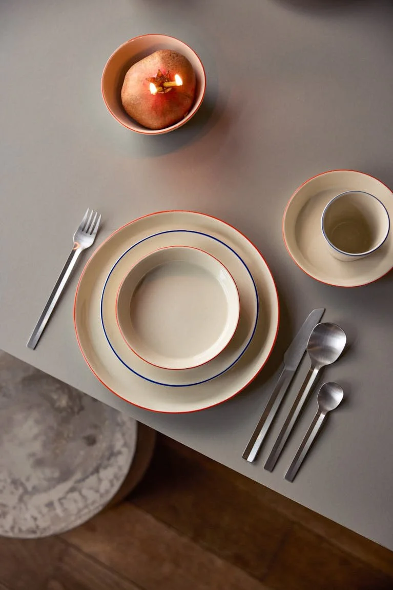 onomao Aberta collection with layered stoneware plates, bowl and cup featuring hand-painted blue and orange rims, photographed for LE MILE Magazine.
