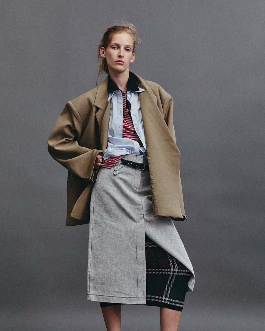 KIRA ALFERINK for LE MILE Magazine Digital Fashion Editorial SS26 photo by Antonio Crotti Kira wears blazer by THE FRANKIE SHOP, shirt and denim skirt by TORY BURCH, t-shirt and tartan skirt by N21 and belt by PAUL SMITH