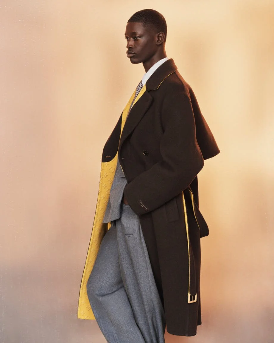 Side view of a model in a brown Louis Vuitton coat with yellow lining, layered over a grey suit.