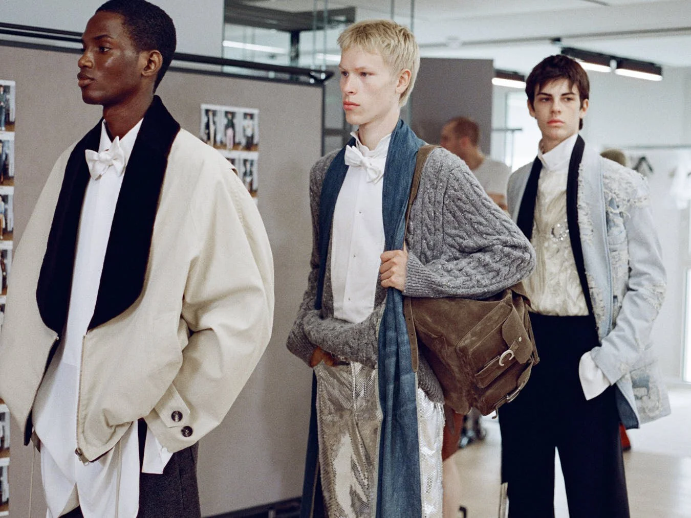 Three models backstage at Dior Men Summer 2027 wearing relaxed formal looks, including a cream jacket with black lapel, a grey knit with silver trousers and a pale embroidered jacket for LE MILE magazine