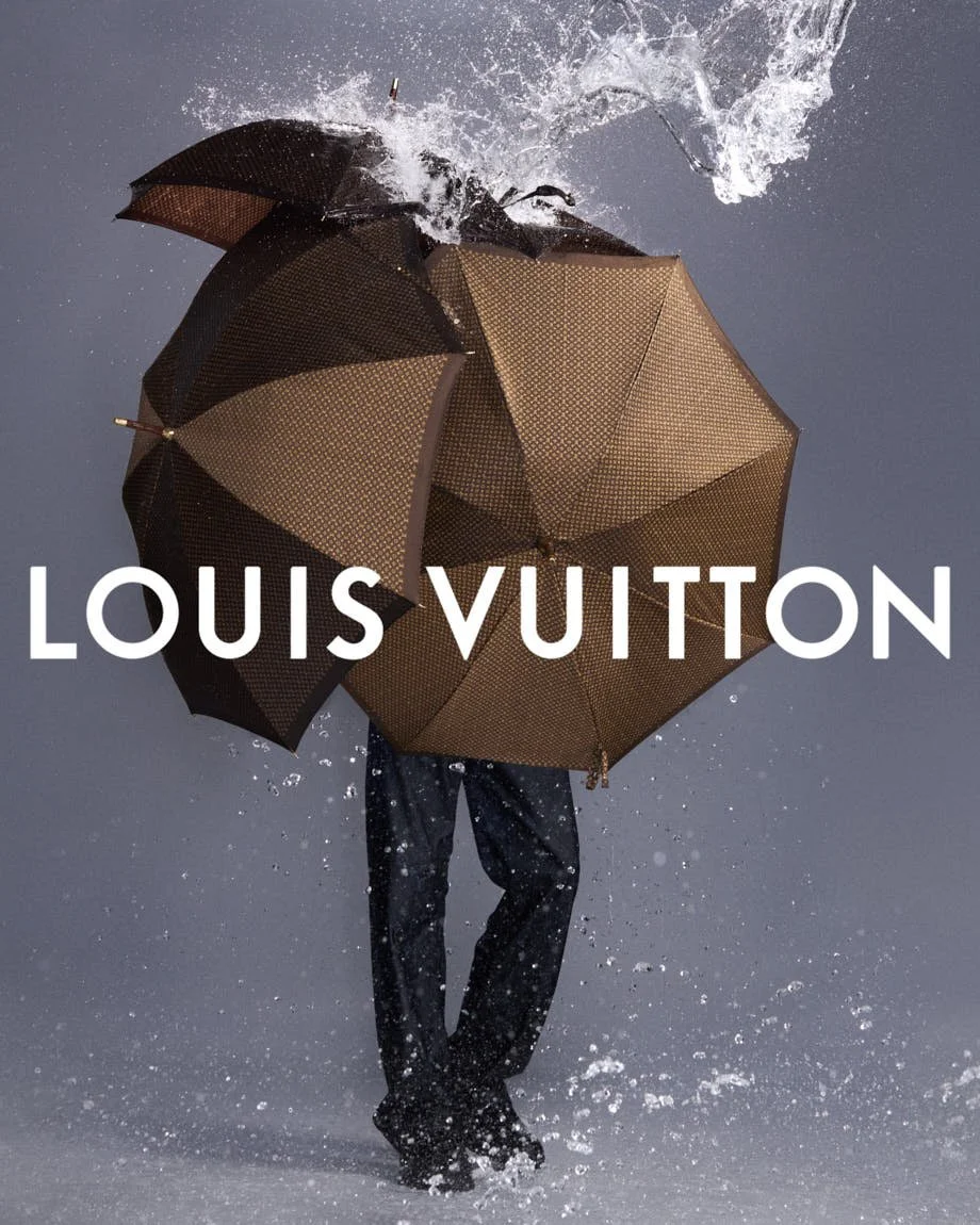 Model obscured by a brown umbrella as water splashes around him in the Louis Vuitton SS27 campaign.