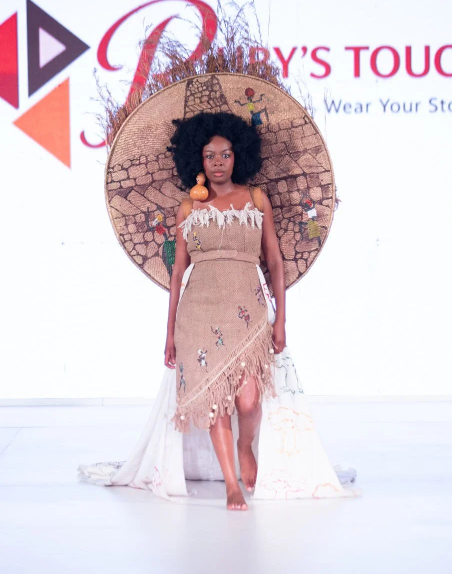 Runway model in a sheer embellished beige dress with a large circular headpiece and delicate decorative detailing.
