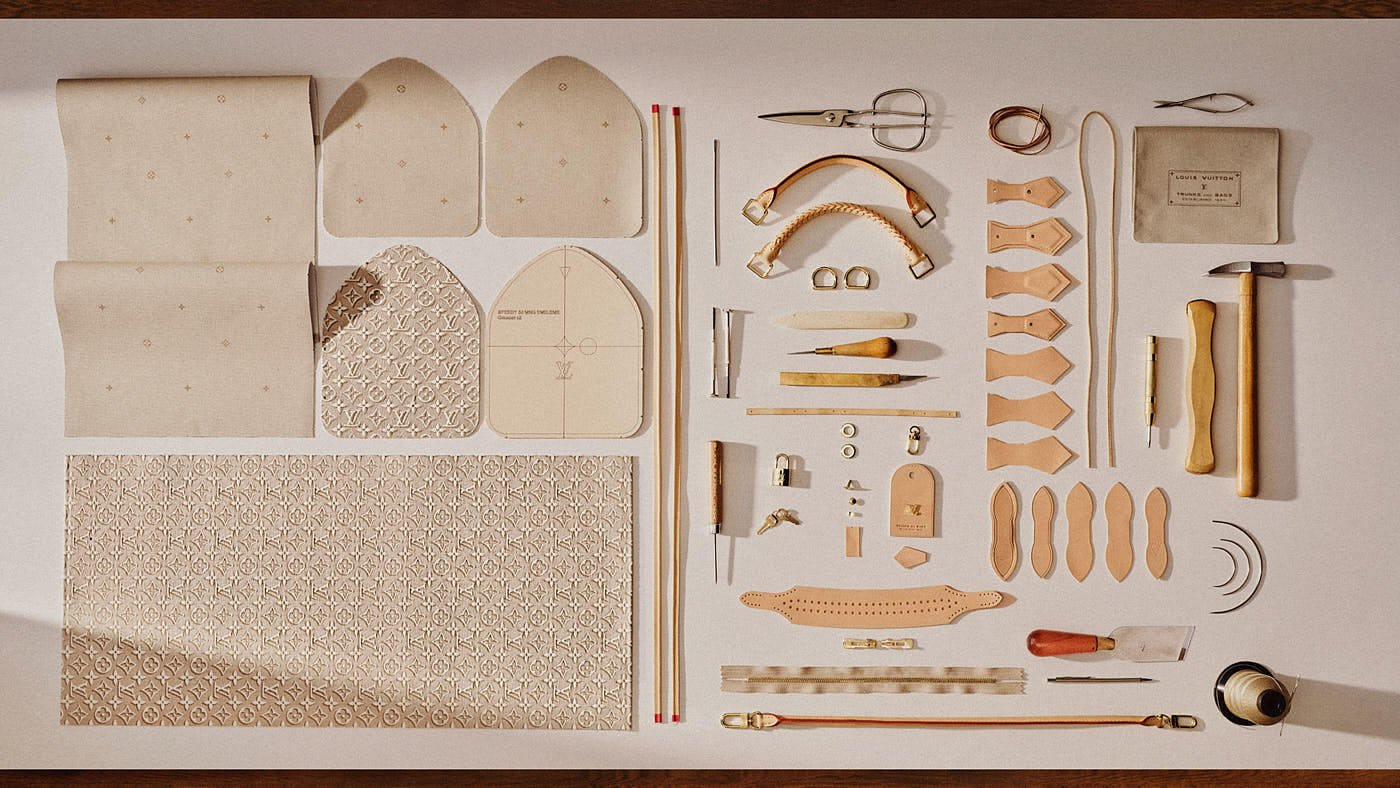 Flat lay of Louis Vuitton Speedy 30 Soft bag components in Monogram Emblème Peuplier, including jacquard canvas panels, leather trims, handles, hardware and artisan tools arranged on a worktable