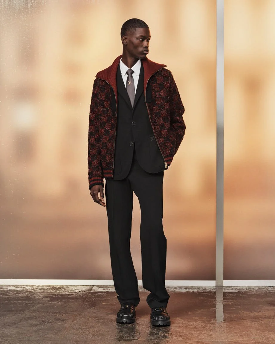 Model wearing a burgundy and black Louis Vuitton jacket over a dark suit, white shirt and tie.