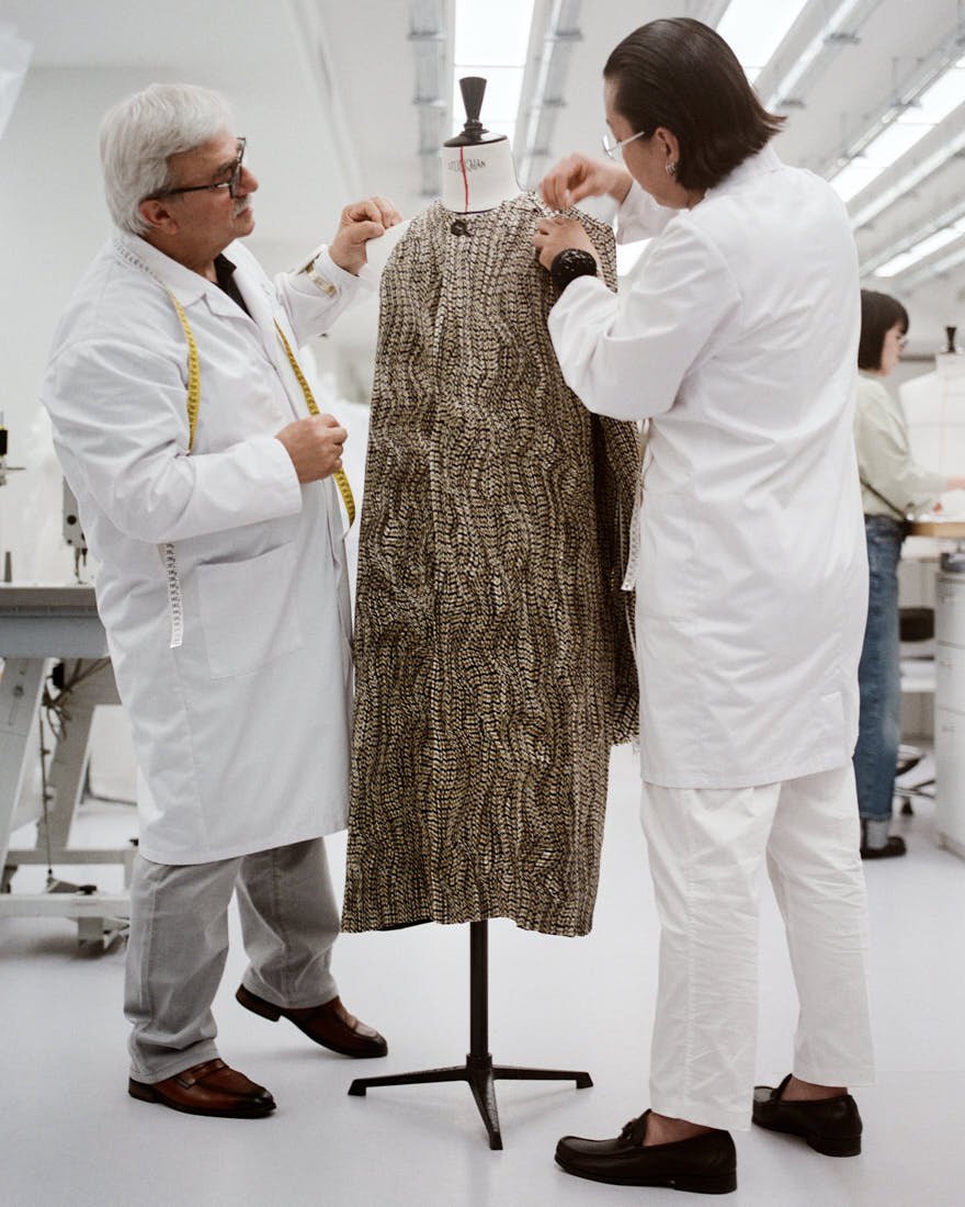 Two Dior atelier workers adjust a textured plissé coat on a mannequin for the Dior Men Summer 2027 collection
