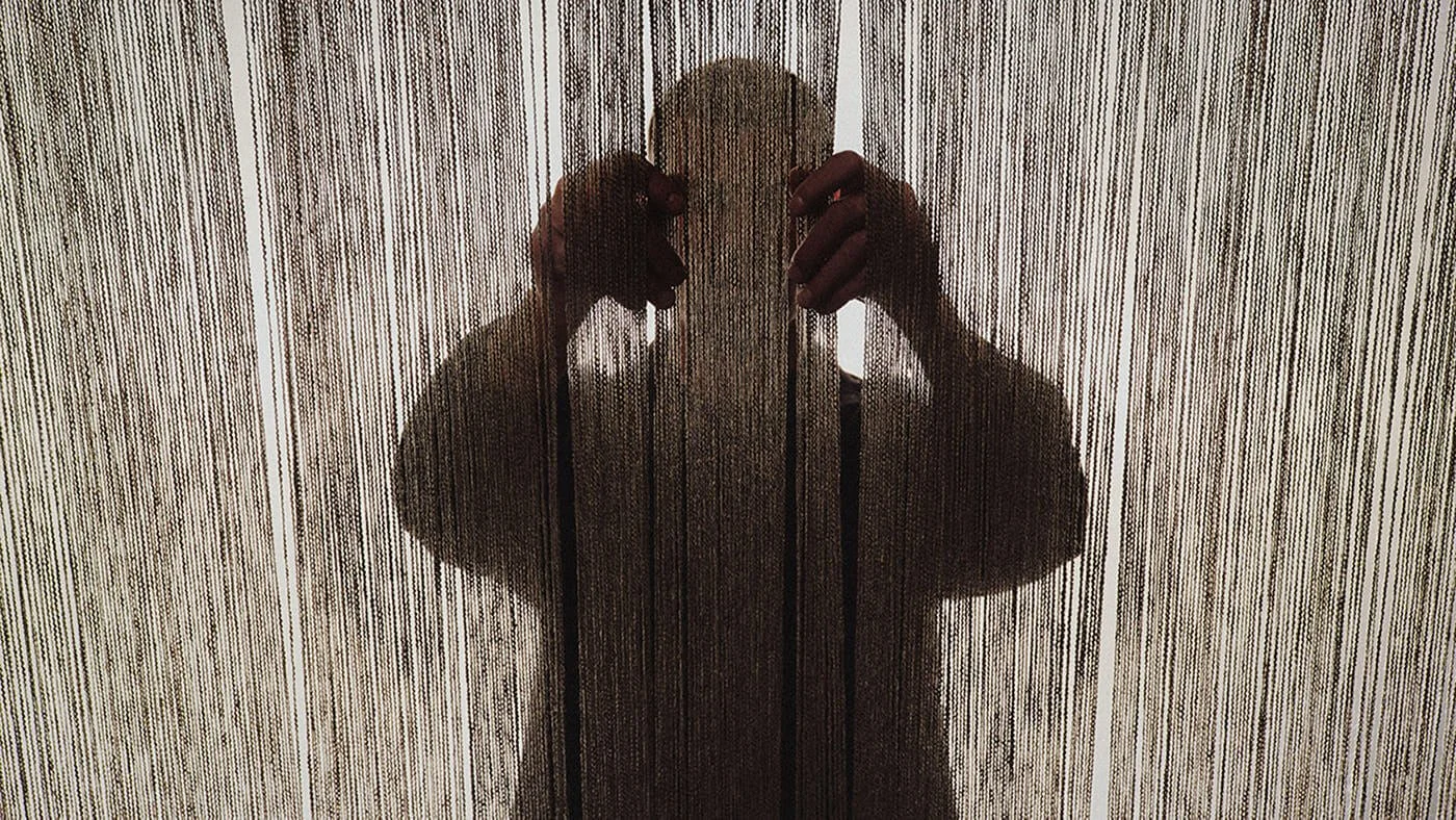 Artisan seen in silhouette behind vertical loom threads while working on the Louis Vuitton Monogram Emblème jacquard canvas