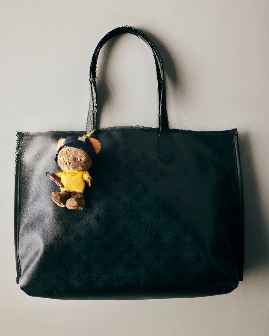 Dark green Louis Vuitton Monogram tote with a bear charm dressed in a yellow raincoat.