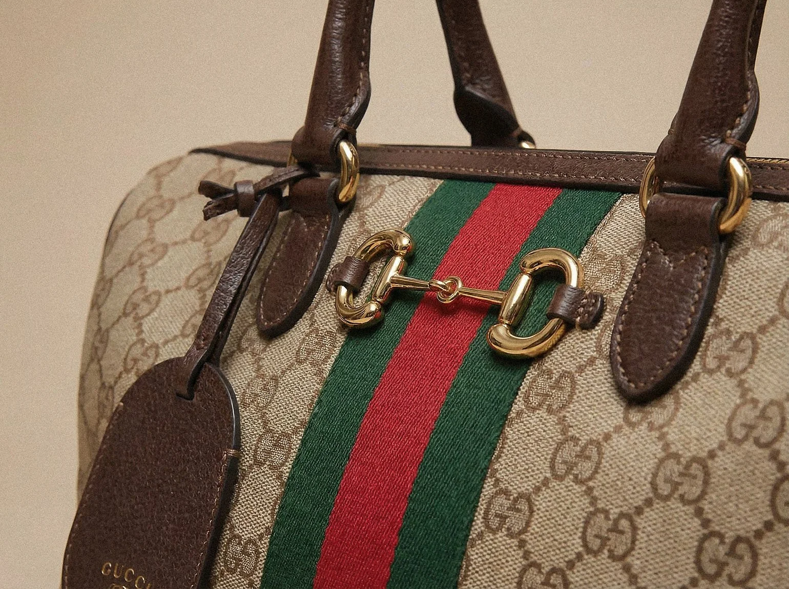 Close-up of a Gucci Borsetto bag in GG Monogram canvas, showing the gold Horsebit hardware, green-red Gucci Web stripe, brown leather handles and leather tag